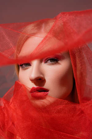Young model with red lips looking at camera near cloth on grey background