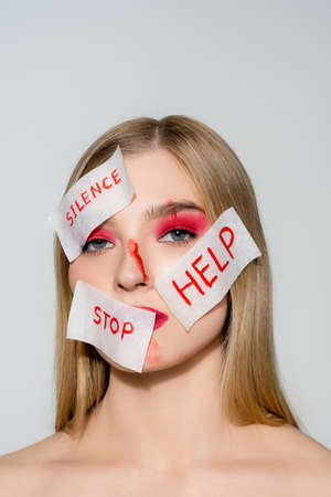 Woman with blood and papers with silence, stop and help lettering on face looking at camera isolated...