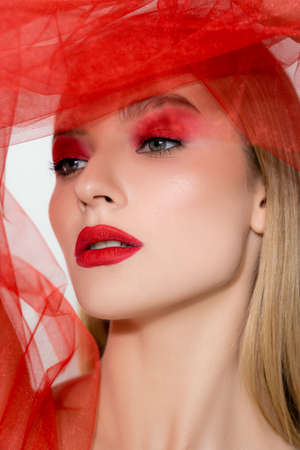 Portrait of model with red lips looking away near tulle cloth isolated on grey