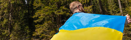 Man holding ukrainian flag in forest, bannerの写真素材
