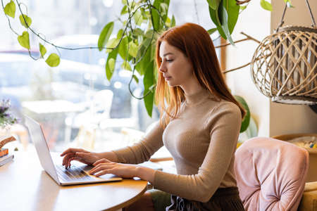 young redhead woman using laptop in cafe
