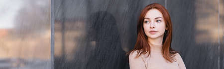 young redhead woman in beige turtleneck near grey marble wall, bannerの写真素材