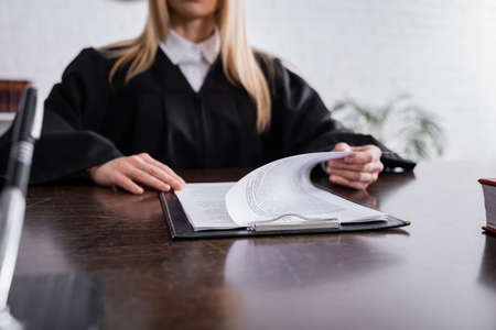 cropped view of prosecutor in black mantle working with papers on blurred background