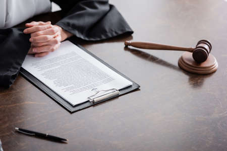 partial view of prosecutor with clenched hands near lawsuit and gavel on wooden desk