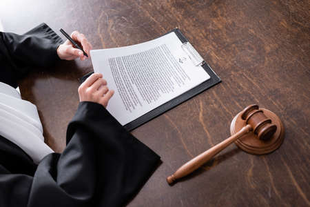 cropped view of judge signing verdict near wooden gavel on desk