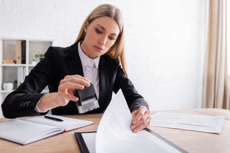 blonde notary holding stamper while working with documents in office
