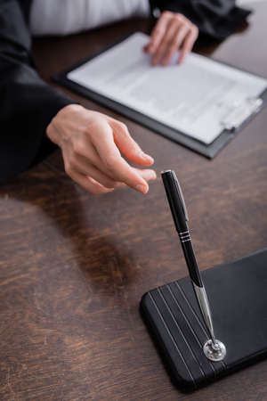 cropped view of prosecutor taking pen while sitting near blurred clipboard
