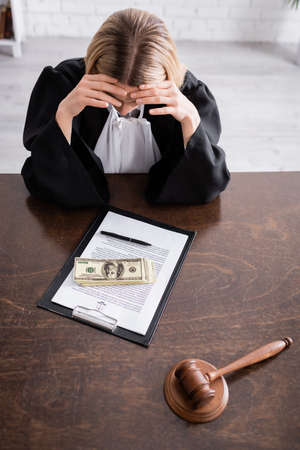 high angle view of prosecutor sitting with bowed head near dollars and lawsuit on clipboard