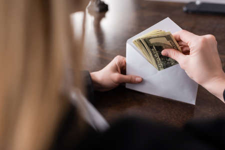 partial view of prosecutor holding envelope and dollar banknotes on blurred foregroundの写真素材