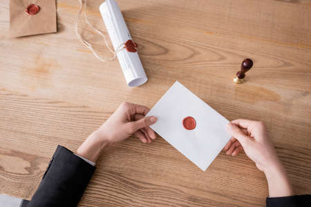 top view of cropped notary holding sealed envelope near stamper and rolled contract