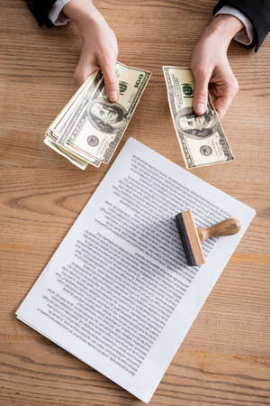 top view of cropped notary counting dollars near contract and stamper