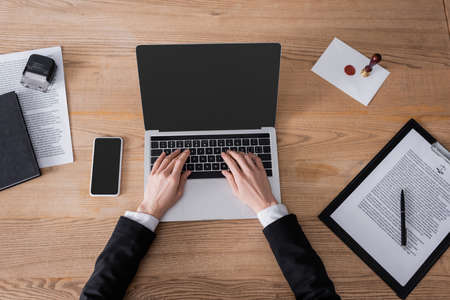 top view of cropped lawyer typing on laptop near smartphone with blank screen and contract