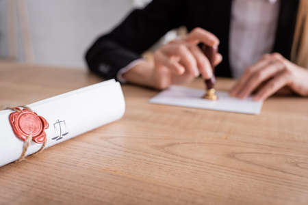 selective focus of rolled contract sealed with wax stamp near cropped notary on blurred background