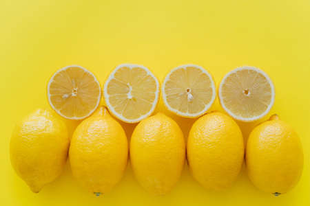Top view of rows of whole and cut lemons on yellow surfaceの写真素材