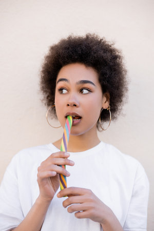 african american young woman in hoop earrings eating jelly strip on white