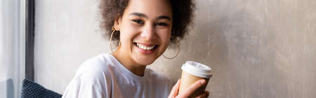 happy african american woman in white t-shirt holding paper cup, banner