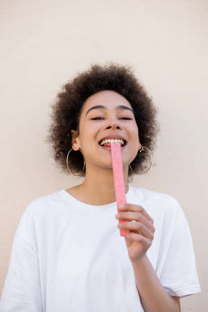 happy african american young woman eating sweet jelly strip on whiteの写真素材