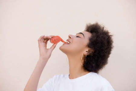 happy african american young woman eating jelly bubble tape on whiteの写真素材