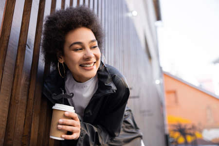 low angle view of cheerful african american woman holding takeaway drink and straw with moustache