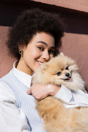 happy african american woman holding in arms pomeranian spitz and looking at cameraの写真素材