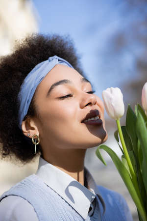 positive young african american woman looking bouquet of tulipsの写真素材