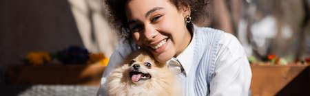 happy african american woman smiling near pomeranian spitz, bannerの写真素材