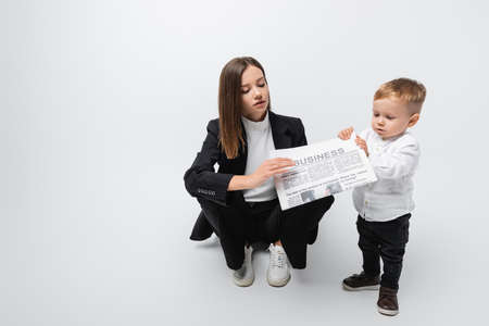 woman in black suit holding newspaper near little son while sitting on greyの写真素材