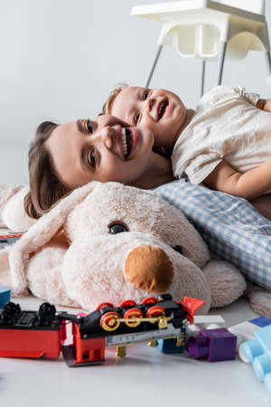 laughing woman looking at camera near son and huge soft toy on greyの写真素材