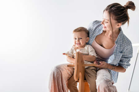 happy boy sitting on rocking horse near young mother on whiteの写真素材
