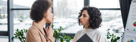 Pensive african american businesswoman looking at flip chart near muslim colleague in office, bannerの写真素材