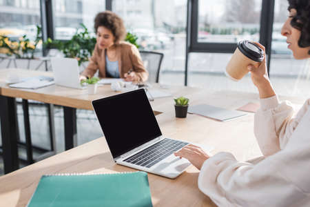 Arabian businesswoman using laptop and holding coffee to go in officeの写真素材