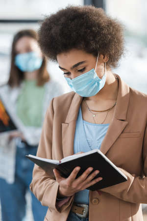 African american businesswoman in medical mask holding notebook in officeの写真素材