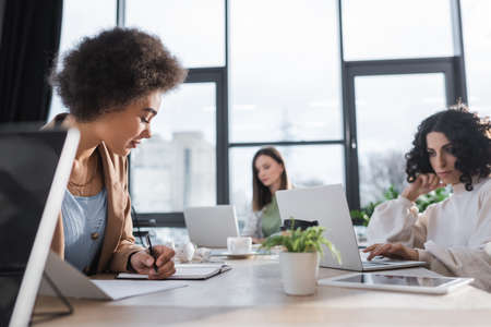 African american businesswoman writing on notebook near multiethnic colleagues in officeの写真素材