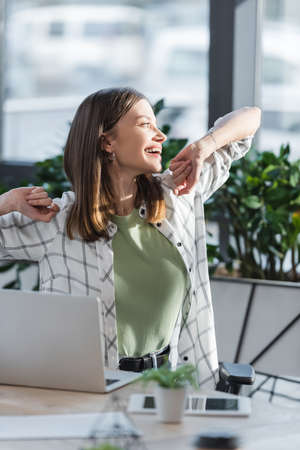 Happy young businesswoman looking away near gadgets in officeの写真素材
