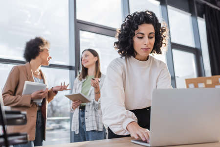 Muslim businesswoman using laptop near blurred multiethnic colleagues talking in officeの写真素材
