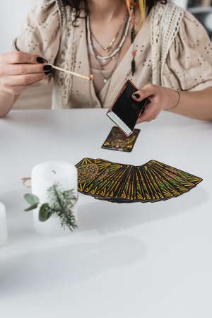 KYIV, UKRAINE - FEBRUARY 23, 2022: Cropped view of fortune teller holding match near tarot cards and candle on tableのeditorial素材