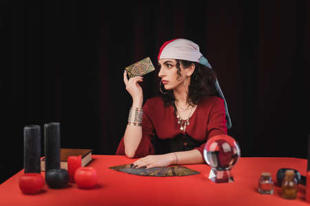 KYIV, UKRAINE - FEBRUARY 23, 2022: Young gypsy fortune teller holding tarot near witchcraft supplies...
