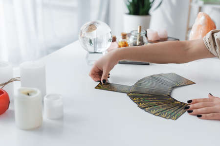 KYIV, UKRAINE - FEBRUARY 23, 2022: Cropped view of fortune teller holding tarot near blurred candles on tableのeditorial素材