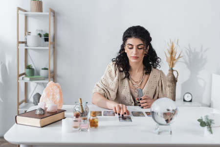 Gypsy fortune teller holding tarot cards near blurred orb on table