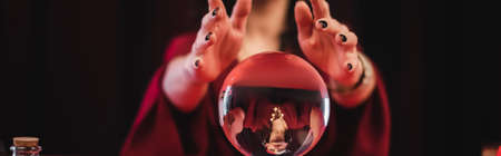 Cropped view of blurred soothsayer and magic orb isolated on black, banner