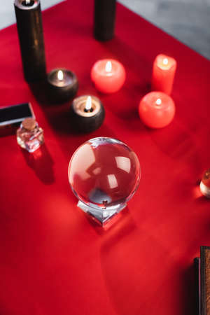 Top view of glass orb near blurred candles and book on table