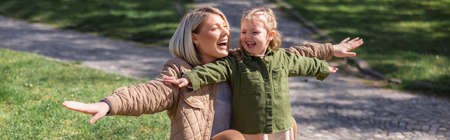 excited mother and daughter with outstretched hands having fun outdoors, banner