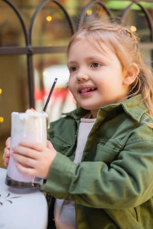 happy girl holding glass with milkshake on blurred foregroundの写真素材