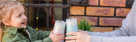 mother and child toasting with glasses of milkshake in cafe outdoors, banner