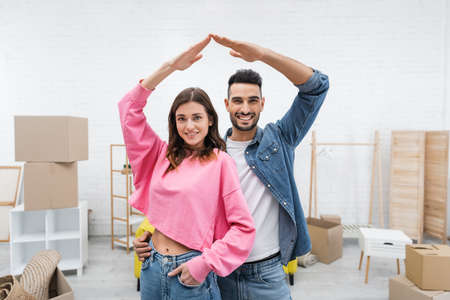 Positive interracial couple looking at camera near blurred carton boxes at home