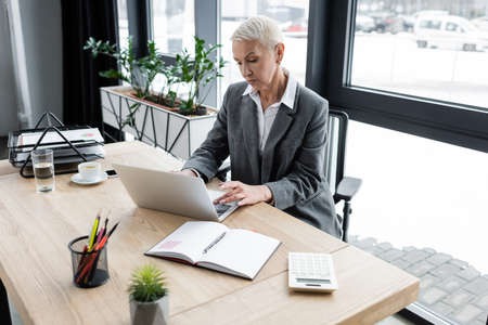 senior accountant typing on laptop near empty notebook and calculatorの写真素材