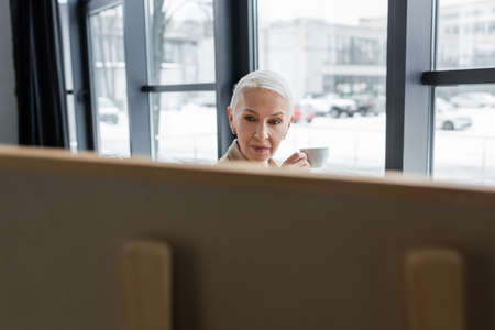 senior banker with short hair holding coffee cup near blurred flip chartの写真素材