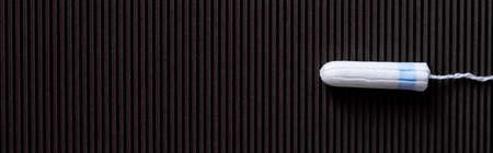 top view of white hygienic tampon on black textured background, banner