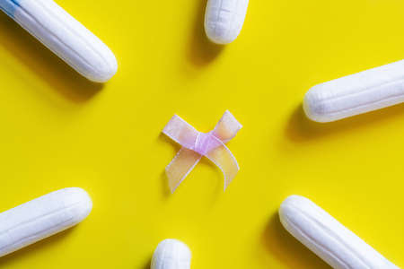 top view of white tampons around bow on yellow background