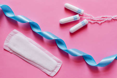 top view of tampons and soft panty liner near blue satin ribbon on pink backgroundの写真素材